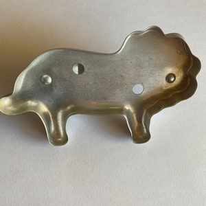 Puede incluir: Un cortador de galletas de metal plateado con forma de le&oacute;n. El cortador tiene una melena detallada y un cuerpo simple.