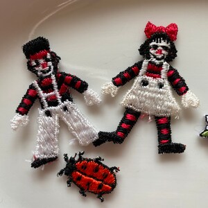 May include: Three embroidered iron-on patches: a black and white striped boy, a black and white striped girl with a red bow, and a red ladybug.