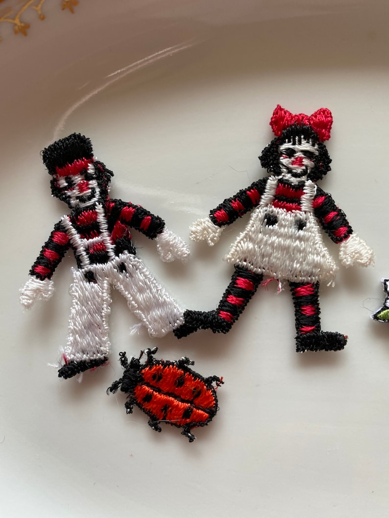 May include: Three embroidered iron-on patches: a black and white striped boy, a black and white striped girl with a red bow, and a red ladybug.