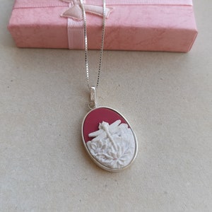 Puede incluir: Un collar de cadena de plata con un colgante de camafeo rojo y blanco con un diseño de libélula.