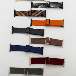 Könnte beinhalten: Eine Sammlung gewebter Apple Watch-Armbänder in verschiedenen Farben, darunter Schwarz, Beige, Grau, Orange, Marine, Braun und Burgunder. Jedes Armband verfügt über eine Schnalle und einen Anschluss für die Uhr. Die Armbänder werden auf weißem Hintergrund präsentiert.