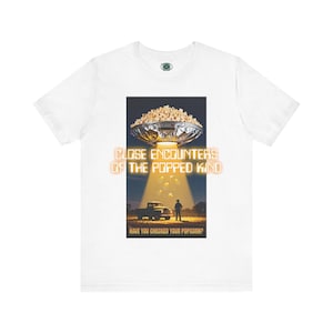 以下が含まれることがあります： 白いTシャツ。UFOが農家とトラックにポップコーンを照射するグラフィック。テキストは「CLOSE ENCOUNTERS OF THE POPPED KIND」と「HAVE YOU CHECKED YOUR POPCORN？」と書かれています。