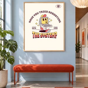 Può includere: Una stampa murale rettangolare in una cornice di legno chiaro raffigurante un personaggio computer a cartone animato con un berretto rosso e un portatile. Il testo recita HAVE YOU TRIED REBOOTING THE SYSTEM? ESTD 1995, con stelle gialle su sfondo crema.