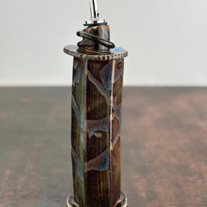 May include: A brown and blue ceramic oil and vinegar bottle with a silver pour spout and a decorative base.