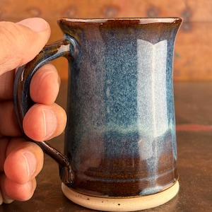 May include: A blue and brown ceramic mug with a white rim. The mug has a speckled glaze and a rounded handle.