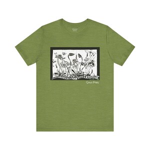 May include: Green t-shirt featuring a black and white floral design within a rectangular frame. The artwork includes stylized flowers and foliage, with the words "Sola Fides" at the bottom right. The shirt is made of a soft material.
