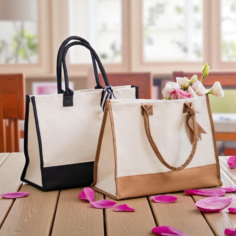 Two stylish handbags, one white and one black, sit on a wooden table with pink flower petals scattered around them.