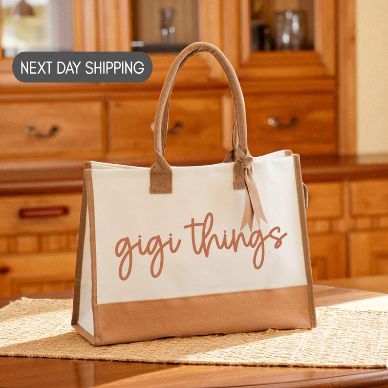 A white tote bag with the text "gigi things" printed on it, placed on a woven placemat on a wooden table.