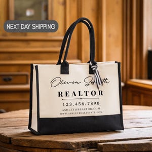 May include: Cream-colored tote bag with black trim and handles. The bag features the name "Olivia Smith" and the word "REALTOR" in black text, along with contact information. A striped ribbon is tied to one of the handles.