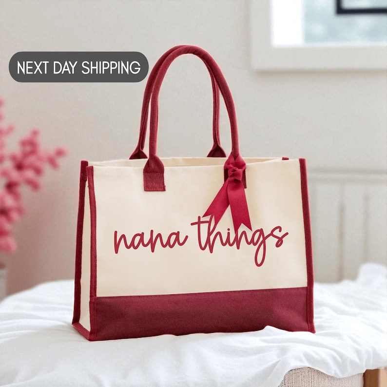 A red and white tote bag with the text "nana things" printed on it, sitting on a white surface.