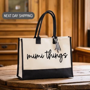 A black and white tote bag with the text "mimi things" printed on it, sitting on a wooden surface.