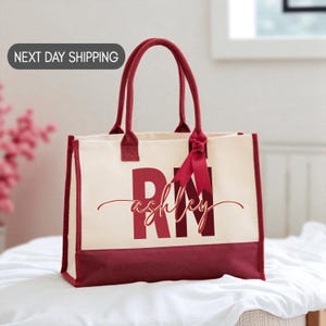 A red and white tote bag with the name "Ashley" printed on it, sitting on a white surface.
