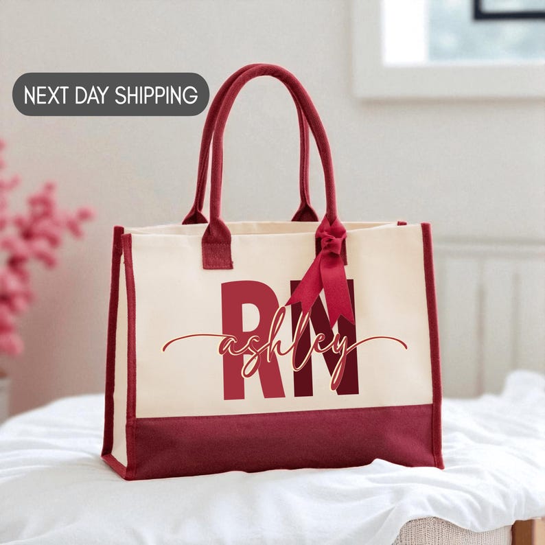 A red and white tote bag with the name "Ashley" printed on it, sitting on a white surface.