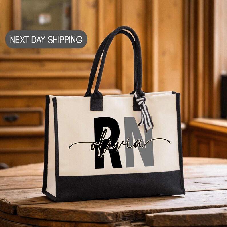 A black and white tote bag with the word "olivia" printed on it, sitting on a wooden surface.