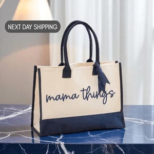 A beige tote bag with the text "mama things" printed on it, sitting on a marble countertop.