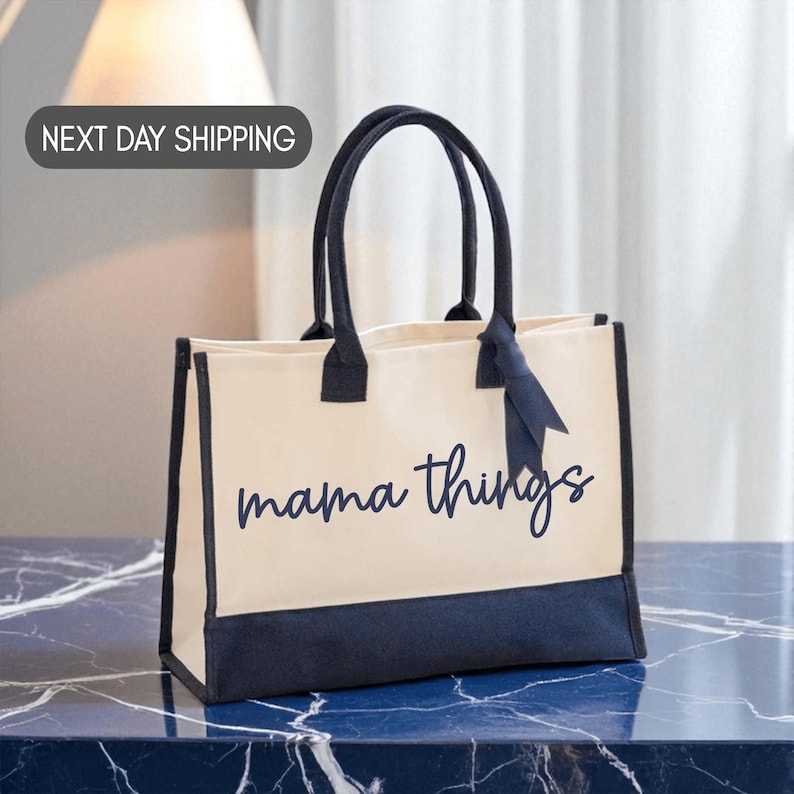 A beige tote bag with the text "mama things" printed on it, sitting on a marble countertop.