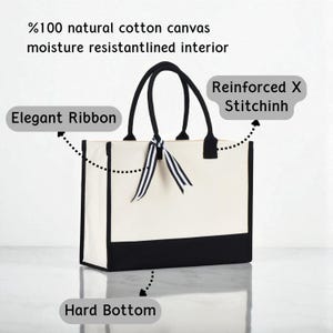 a white tote bag with a black and white ribbon tied around it, and it has a hard bottom.