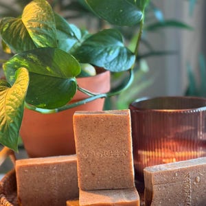 May include: A stack of rectangular, textured brown soap bars with the word GOGREEN embossed on the front. The soap bars are arranged in a woven basket, featuring a speckled appearance with visible particles throughout the surface of each bar.