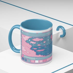 May include: A white ceramic mug with a blue handle and interior. The mug features a pastel landscape design with pink clouds, a blue sea, and stars. The mug has a blue rim and a decorative design.