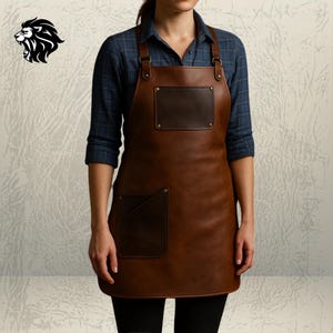 Könnte beinhalten: Braune Lederschürze mit zwei Vordertaschen und einer Brusttasche. Die Schürze hat verstellbare Träger und ist für den Einsatz in einer Küche oder Werkstatt konzipiert. Sie besteht aus strapazierfähigem Material.