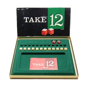 May include: A green game board with the words "Take 12" printed on it. The board has a row of numbered tiles from 1 to 12. There are also two red dice and a smaller card with the words "Take 12" printed on it.