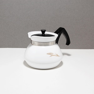 May include: A white teapot with a rounded body, a black handle, and a black lid. A metallic silver band encircles the upper portion of the pot. A gold-colored wheat stalk graphic is printed on the side of the white body of the teapot.