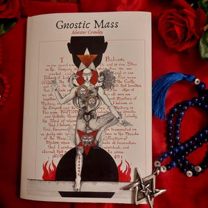 May include: A book titled "Gnostic Mass" by Aleister Crowley, featuring an illustration of a figure with multiple faces and symbols. The image is set against a red backdrop with a rosary, a star pendant, and roses.
