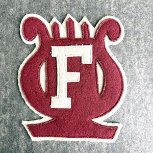 May include: A maroon felt patch with a white outline in the shape of a lyre with the letter "F" in the center.