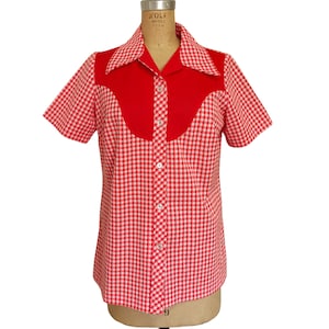 May include: A short-sleeved shirt with a red and white gingham pattern. The shirt features a solid red yoke and collar, with white buttons down the front. The shirt is displayed on a mannequin.