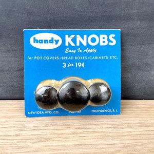 May include: A blue and white package of three black wooden knobs. The package says "handy KNOBS Easy To Apply for POT COVERS BREAD BOXES CABINETS ETC. 3 for 19¢ NEW IDEA MFG. CO. PROVIDENCE, R. I."