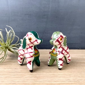 May include: Two ceramic salt and pepper shakers shaped like dogs. The shakers are green and white with red plaid accents. They have a stitched design and a maple leaf with "Parry Sound, Canada" written on a banner.