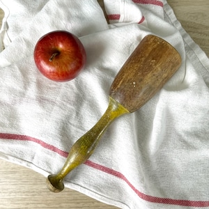 May include: A wooden potato masher with a yellow painted handle. The masher is on a white kitchen towel with red stripes.