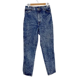 May include: Acid wash denim jeans hanging on a wooden hanger. The jeans have a high waist and a classic five-pocket design. The denim is a medium blue with a distinctive white, marbled pattern.