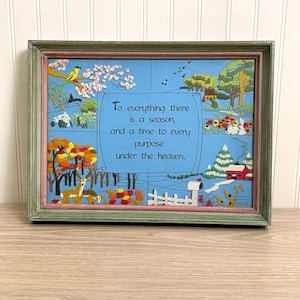 May include: A framed embroidery art piece featuring a central scroll with the text To everything there is a season, and a time to every purpose under the heaven. The design depicts four seasonal landscapes with trees, flowers, a deer, and a house.