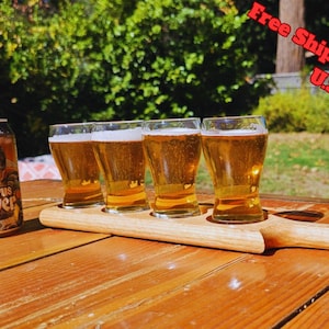 May include: A wooden beer flight with four glasses of beer and a can of Citrus Slayer IPA. The beer glasses are filled with a golden-colored liquid. The can has a cartoon graphic of a character in sunglasses.