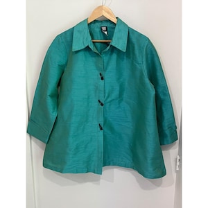May include: A teal button-down shirt with a textured finish, featuring a pointed collar, three-quarter length sleeves with cuffs, and three black toggle-style closures down the front. The garment has a flared silhouette and a visible brand label.