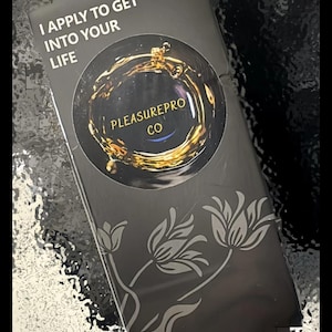 Pode incluir: Uma caixa retangular preta com o texto "I APPLY TO GET INTO YOUR LIFE" e o logotipo de "PLEASUREPRO CO". A caixa tem um design floral e detalhes dourados.