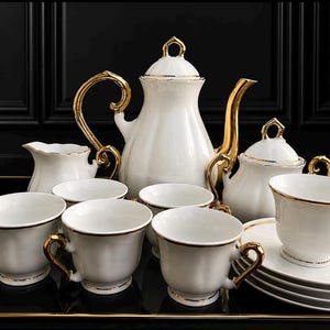 May include: A white porcelain tea set comprising a teapot, a lidded sugar bowl, a creamer, and several teacups with matching saucers. Each piece is finished with gold trim on the rims, handles, and lids, featuring a fluted, elegant design.