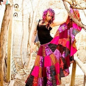 May include: A woman wearing a long, multi-colored patchwork skirt with a black tank top. The skirt is made of various fabrics in shades of pink, purple, and black.
