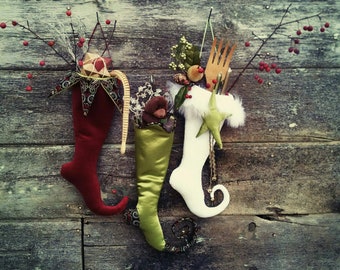 May include: Three Christmas stockings hanging on a rustic wooden wall. The stockings are decorated with different colors and patterns, including red, green, white, and gold. The stockings are filled with various items, including a stuffed animal, a wooden spoon, and a small gift box.