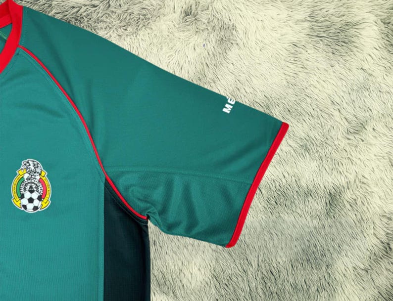 May include: Green soccer jersey with red trim and the Mexican national team emblem on the chest. The jersey has a dark green panel on the side and the word "ME" printed on the sleeve.
