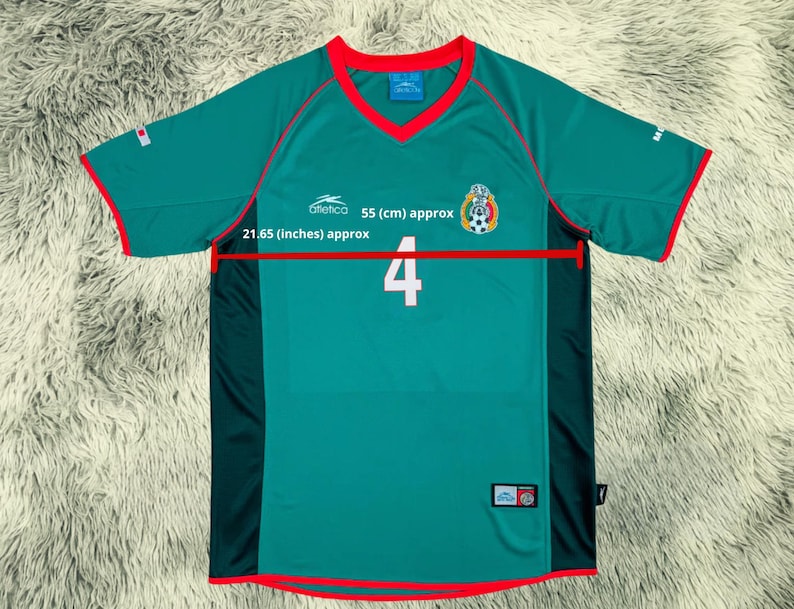 May include: A green soccer jersey with red trim, a V-neck, and short sleeves. The jersey features the number 4 in white, a team emblem, and the text "Atletico 55 (cm) approx 21.65 (inches) approx".