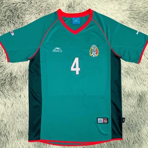May include: A green soccer jersey with red trim and the number 4 in white. The jersey features the Mexican national team emblem and the brand name "Atletica". The jersey is made of a breathable material.