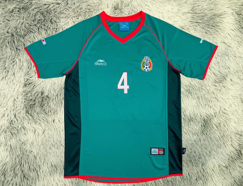 May include: A green soccer jersey with red trim and the number 4 in white. The jersey features the Mexican national team emblem and the brand name "Atletica". The jersey is made of a breathable material.