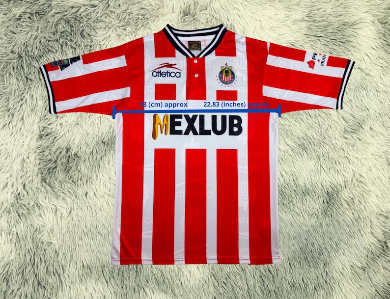 May include: Red and white striped soccer jersey with the word "MEXLUB" in gold letters. The jersey has a white collar and the "Atletica" logo. The sleeves are red and white striped with black trim. The sleeve length is approximately 22.83 inches.