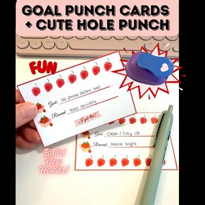 May include: Goal punch cards with a cute hole punch. The cards have strawberry illustrations and text that reads "Goal: No phone before bed" and "Reward: Meal delivery". A purple and blue heart-shaped hole punch is also visible.