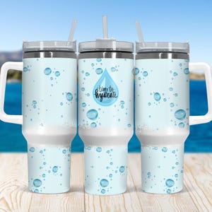 Puede incluir: Tres vasos de acero inoxidable con un diseño de gota de agua azul y blanca. El vaso del centro tiene el texto "time to hydrate" en la gota de agua.