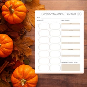 May include: Thanksgiving Dinner Planner on a wooden surface with pumpkins, leaves, and cinnamon sticks. The planner has sections for meal plans and grocery lists. The text "Thanksgiving Dinner Planner" is at the top.