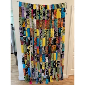 Puede incluir: Una colorida cortina de patchwork con una variedad de tiras de tela estampada. La cortina presenta una mezcla de colores vibrantes que incluyen amarillo, azul, verde y naranja. El diseño incluye patrones florales y geométricos, creando un artículo de decoración del hogar único y artístico.