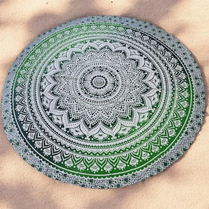 May include: Round green and white mandala beach towel. The towel features a detailed floral design with a gradient effect, transitioning from a dark green center to a lighter green edge. The towel is on a sandy surface.